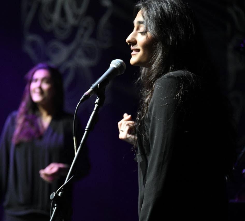 Cantaora ante el micrófono, iluminada en morado, con una segunda artista al fondo